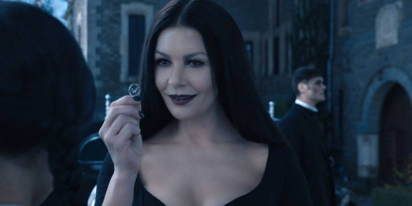 Morticia showing Wednesday something in her hand.