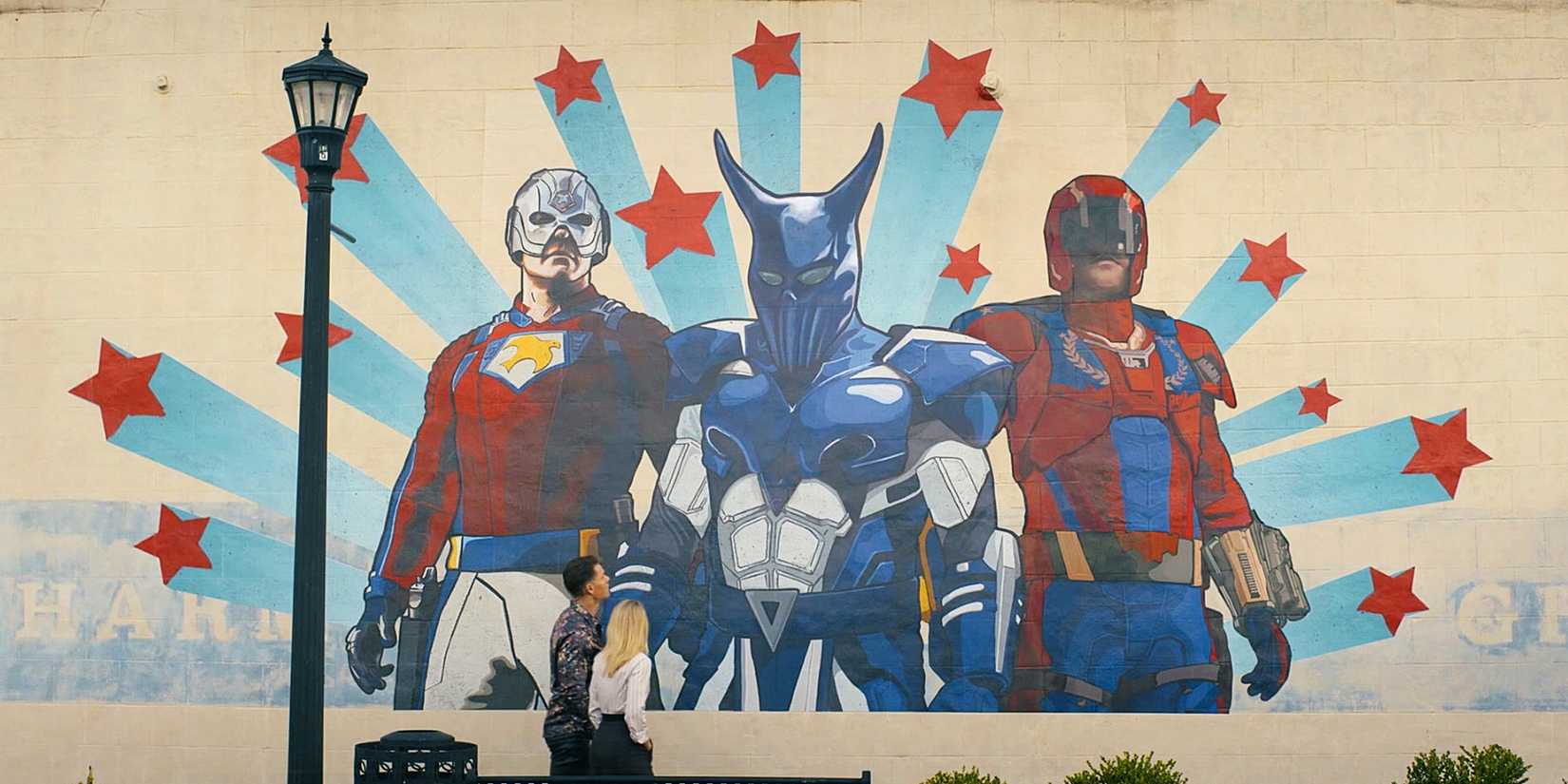 Chris Smith and Alternate Emilia Harcourt walking past the mural of the Top Trio on a wall in Peacemaker Season 2