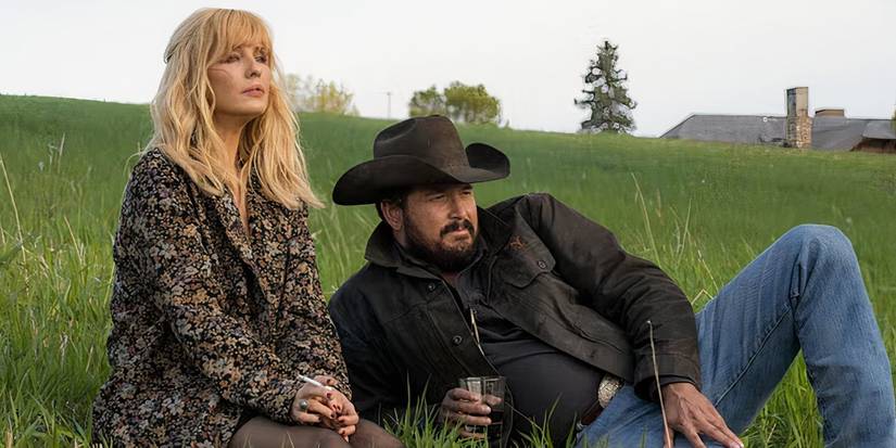 Rip and Beth from Yellowstone sit together in a field.