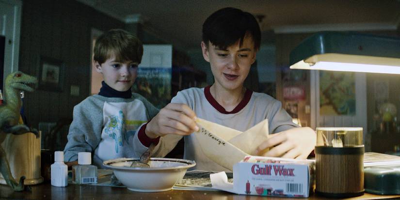 Georgie stands behind Bill as he makes a paper boat in IT (2017)