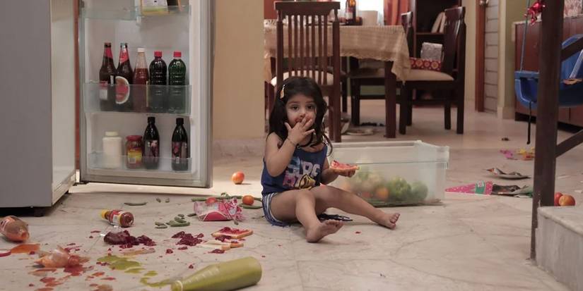 Pihu sitting on the floor in front of the open refrigerator with food all over