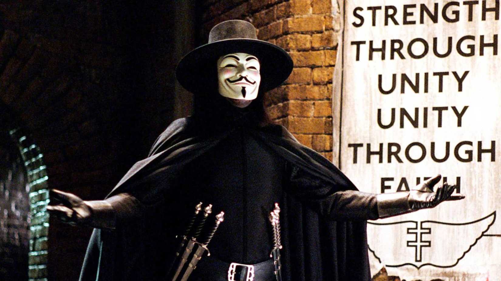 V in full costume, arms spread in front of a fascist poster from V for Vendetta