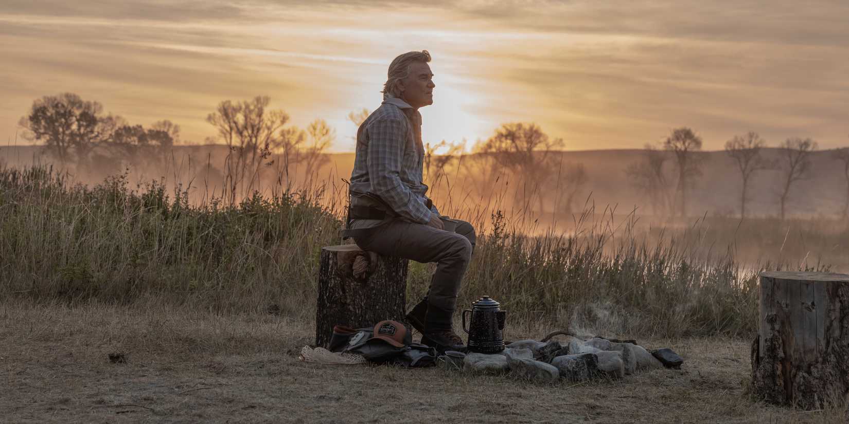 Kurt Russell sits on a tree stump against the sunrise in The Madison