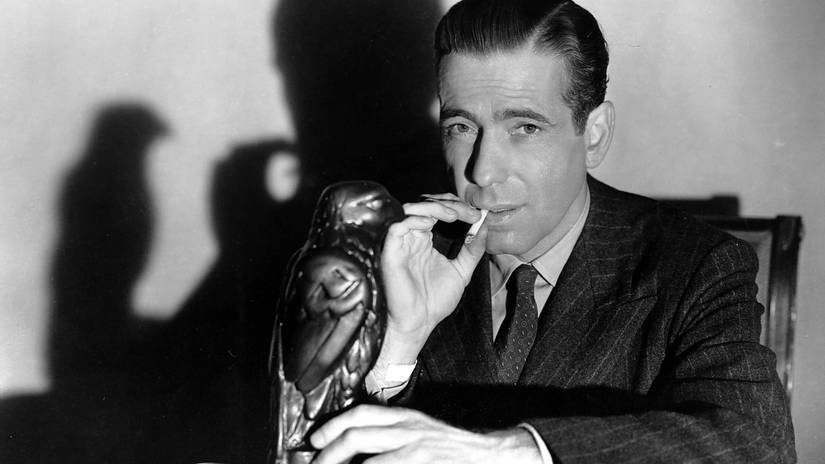 Sam Spade sits at his desk with the maltese falcon