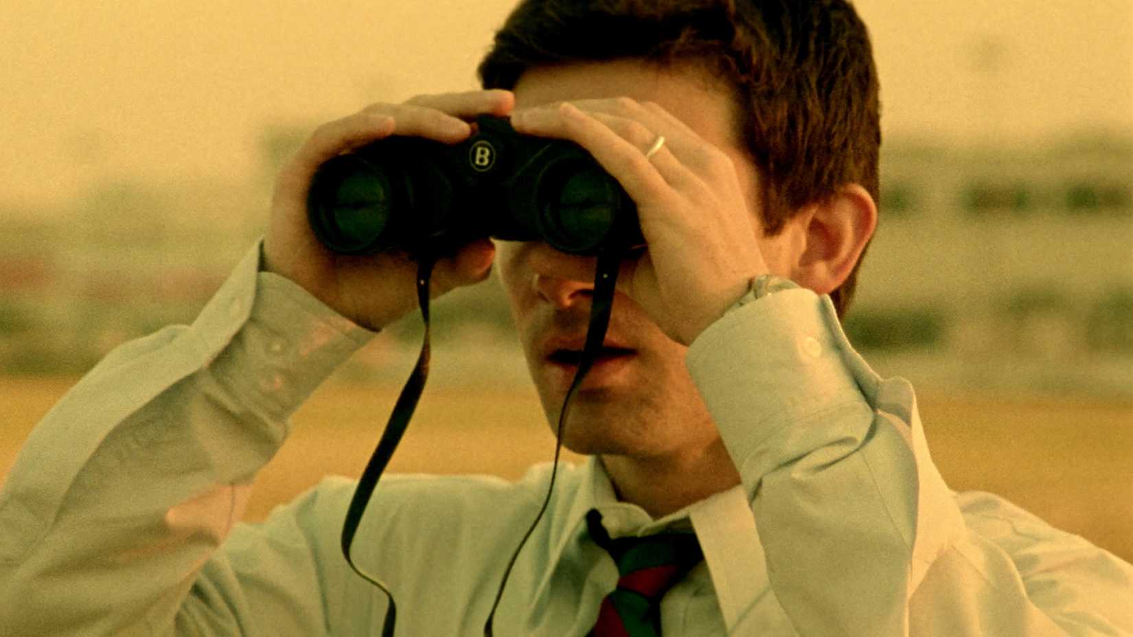Shane Carruth looks through binoculars in Primer
