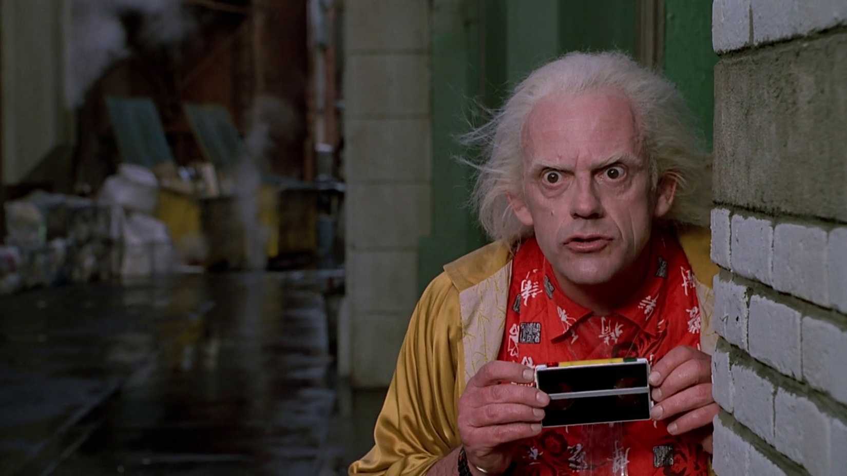 Christopher Lloyd nei panni di Doc Brown nascosto in un vicolo con una macchina fotografica in Ritorno al futuro II