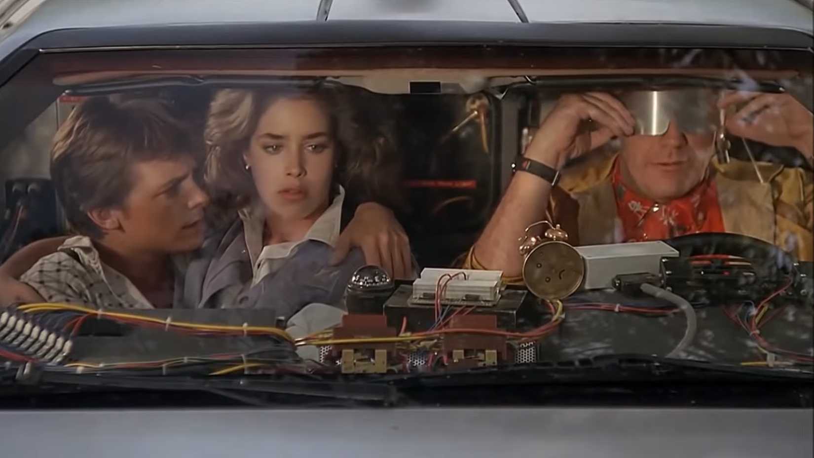 Christopher Lloyd nei panni di Doc Brown seduto accanto a Michael J. Fox nei panni di Marty nella DeLorean in Ritorno al futuro