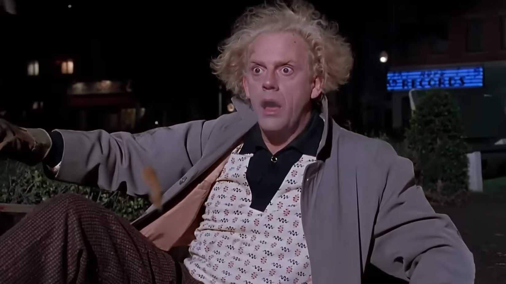 Christopher Lloyd nei panni di Doc Brown, seduto per strada con un'espressione sconvolta in Ritorno al futuro