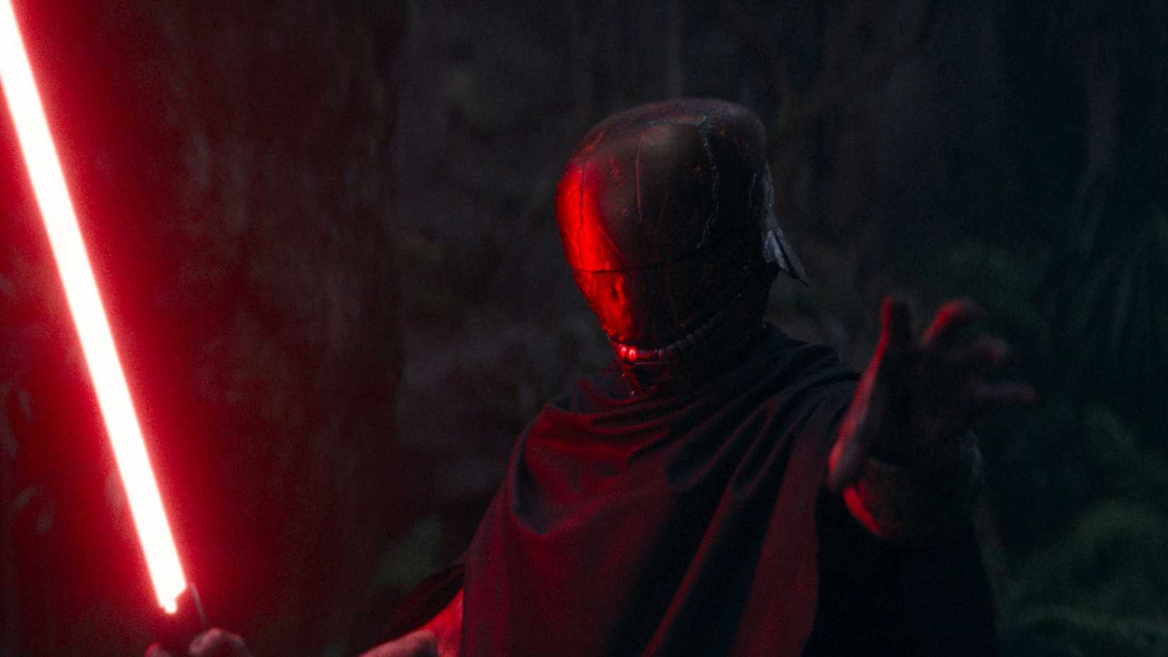 Manny Jacinto as Qimir in The Stranger's disguise with a red lightsaber from The Acolyte