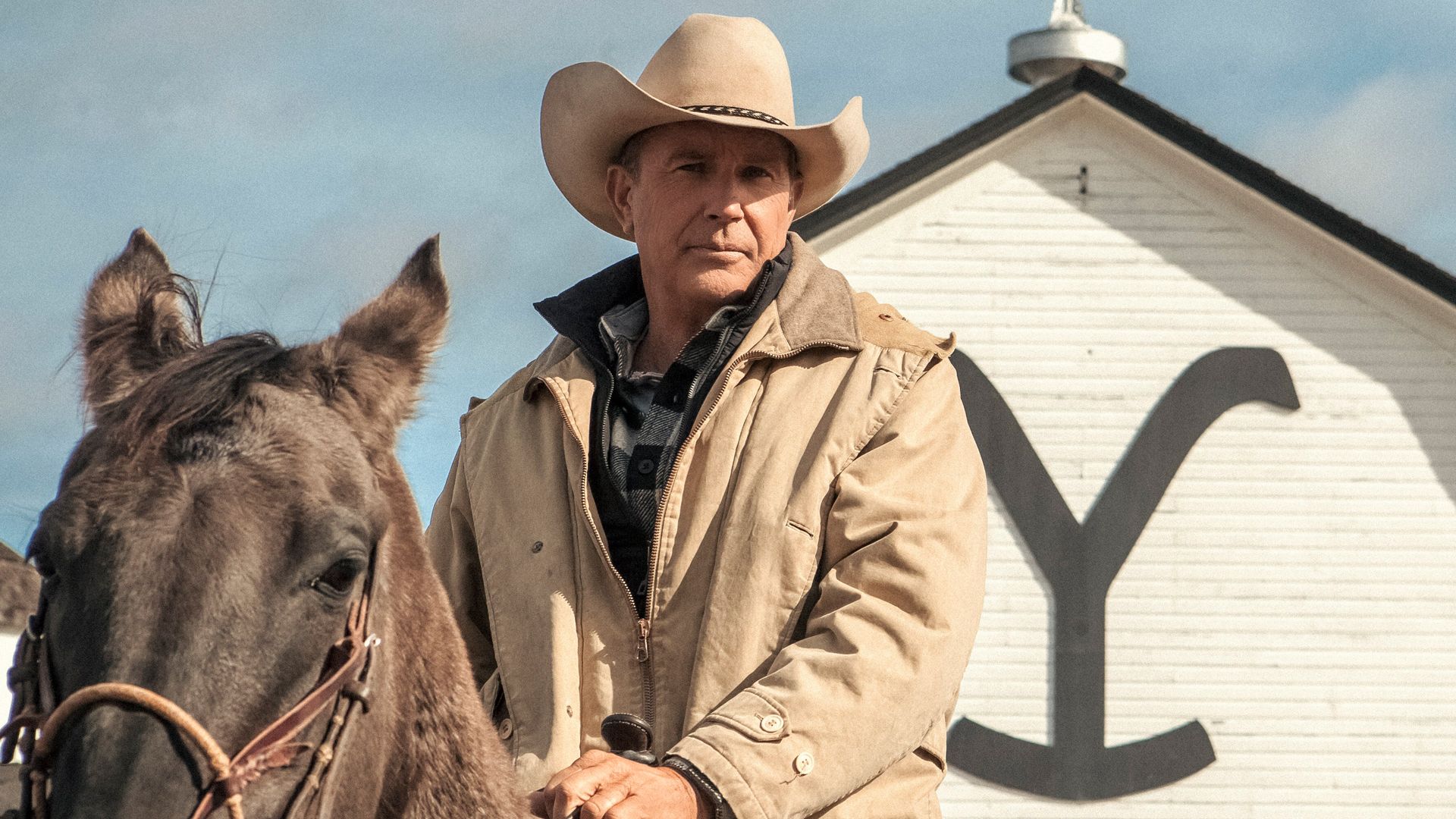 Kevin Costner as John Dutton on horseback with the iconic Yellowstone barn in the background