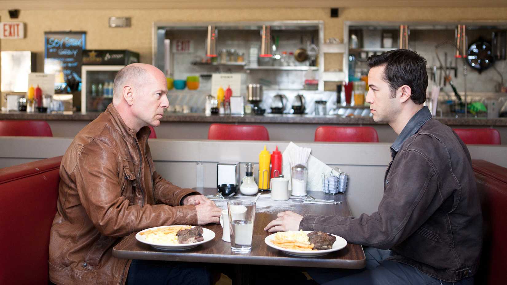 Bruce Willis and Joseph Gordon-Levitt stare at each other in a diner in Looper.
